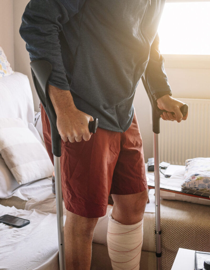 man with bandaged leg and crutches in living room