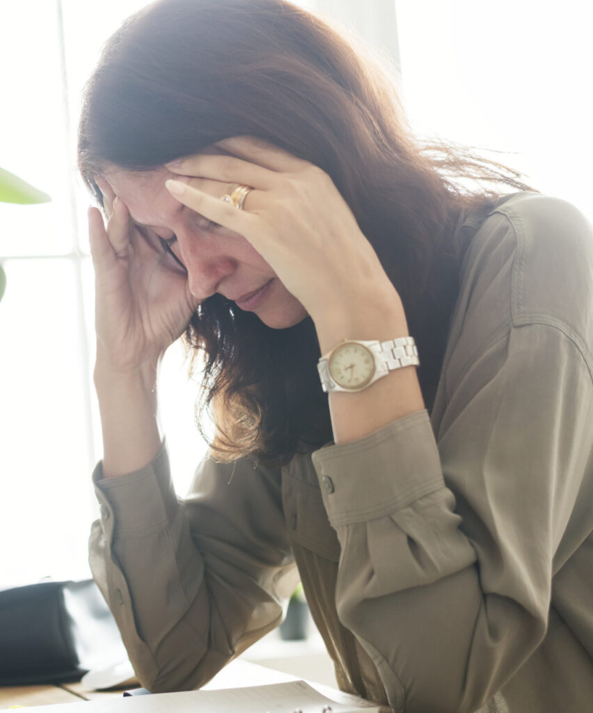 Woman hunched over desk holding head from migraine